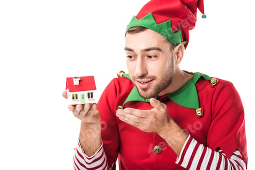 Preview: man in christmas elf costume pointing at house model isolated on white, real estate sale and