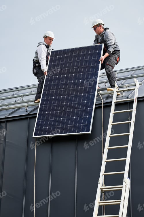 Preview: Workers lifting up photovoltaic solar module while installing solar panel system on roof of house.