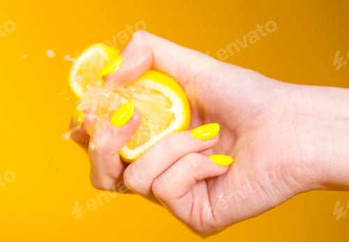 Vista previa: mano con uñas amarillas machacando un limón fresco y jugoso