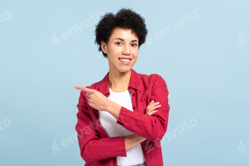 Preview: Cheerful beautiful African American woman pointing finger on copy space isolated on blue background