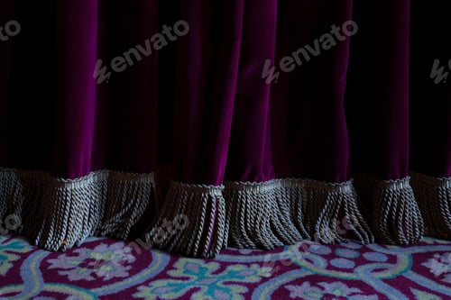 Preview: Folds and fringe of a burgundy colored velvet curtain in an old theater