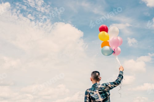 Preview: back of Happy young hipster man holding colorful balloons in grassland enjoy life and happy.