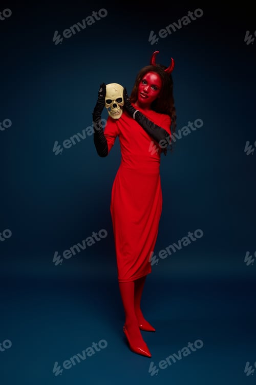 Preview: A captivating woman in a devil costume holding a skull during a Halloween celebration in October