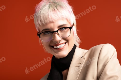 Preview: Young woman with stylish glasses and pastel hair smiles brightly against a vivid orange background