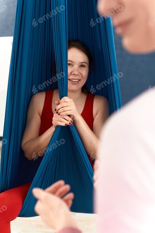 Preview: Young pregnant woman doing exercises of aerial yoga in hammock.