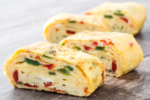 Preview: Tamagoyaki slices with red and green peppers resting on wooden board
