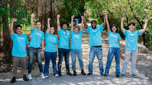 Preview: Group of volunteers for charity join hands and arm around in the forest park area.