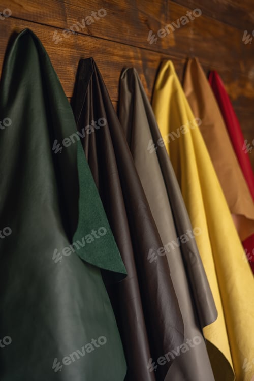 Preview: Genuine leather of different colors for the production of clothes and shoes hangs on a wooden wall.