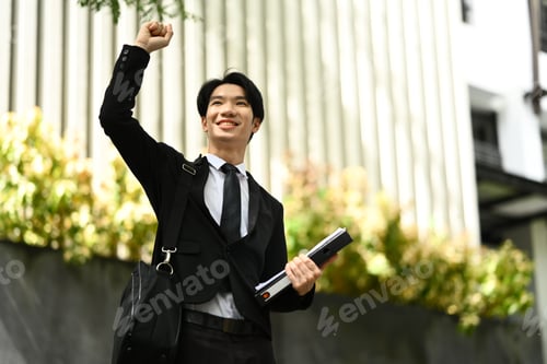 Preview: Low angle view of happy young businessman celebrating victory and successful achievement.