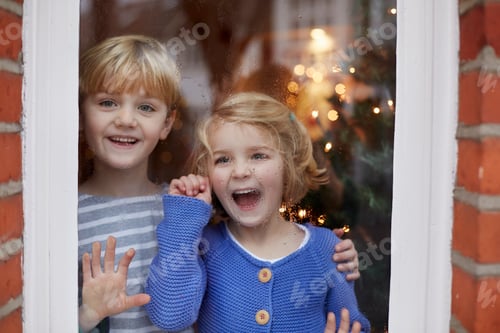 Preview: Two children, a boy and girl, looking out of a window at home with excited expressions.