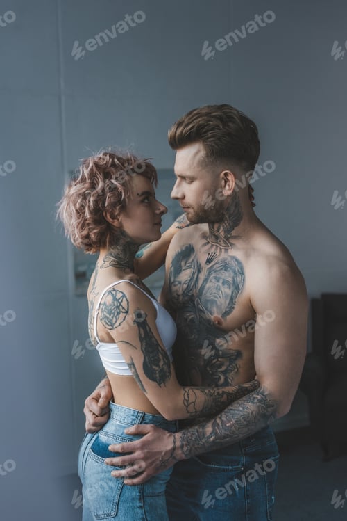 Preview: young tattooed couple embracing in bedroom