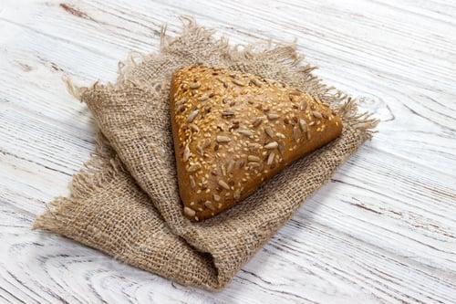 Preview: Fresh baked bread or bun with sesame and sunflower seeds on wooden table