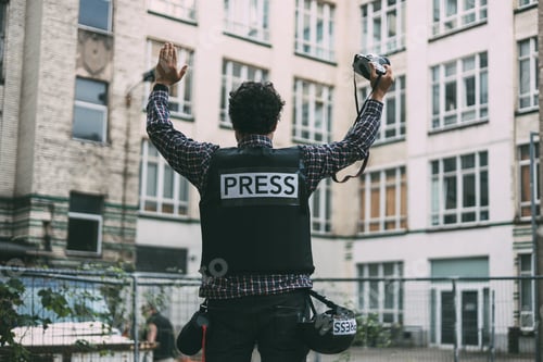 Preview: Photojournalist in bulletproof vest holding his camera with his hands in the air
