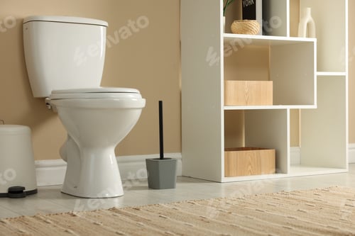 Preview: Toilet bowl, brush and trash bin near beige wall in restroom