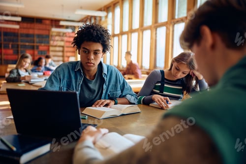Preview: Black student and his friends learning in library at high school.