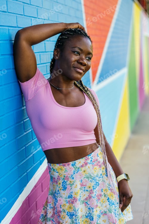 Preview: A woman in a pink shirt and floral skirt poses in front of a colorful wall