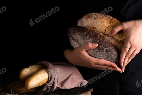 Preview: Close-up of woman hands as heart take fresh bread. Dark photo