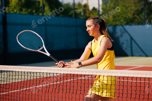 Preview: Focused Young Female Tennis Player Practicing at Net on Outdoor Court in Yellow Dress