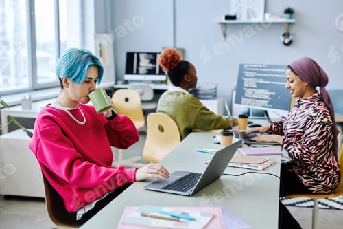Preview: Asian young man using laptop in office and drinking coffee, magenta accent
