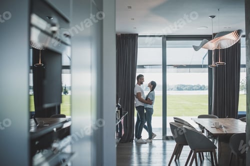 Preview: distant view of handsome adult man embracing attractive girlfriend at home