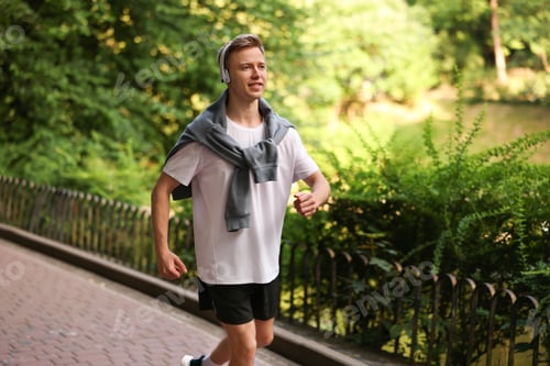 Preview: Smiling sportsman in headphones running outdoors. Morning exercise