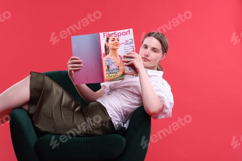 Preview: Woman with lifestyle magazine on armchair against red background, space for text