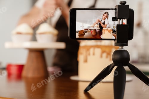 Preview: Camera footage of focused baker woman making cakes with cream in kitchen