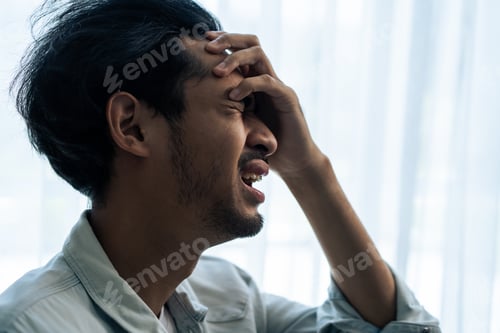 Preview: Asian young upset depressed man sitting alone in living room at home.