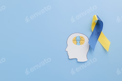 Preview: Puzzle pieces in a paper head and yellow-blue ribbon symbolize Down Syndrome awareness.