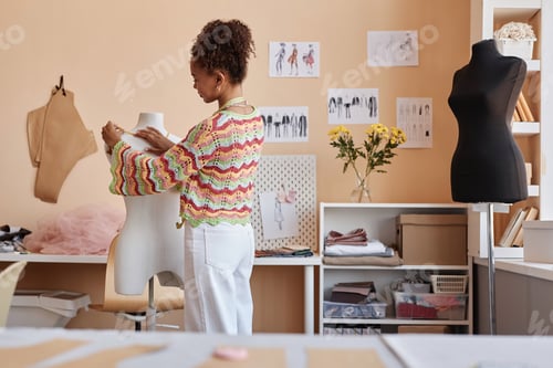 Preview: Young female stylist standing in front of mannequin in workshop
