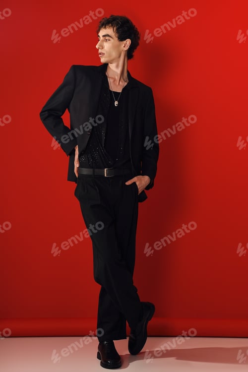 Preview: Stylish man in elegant black attire poses confidently against a bright red backdrop