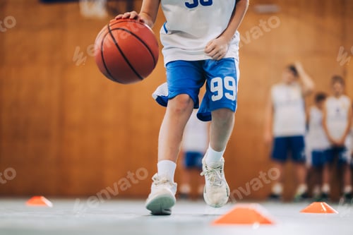 Preview: Cropped picture of a junior athlete dribbling basketball on court.