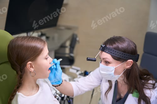 Preview: Doctor in protective gloves and mask examines throat of child