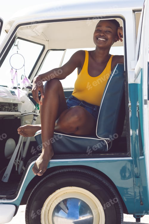 Preview: Front view of happy African american woman looking at camera while sitting in a camper van at beach