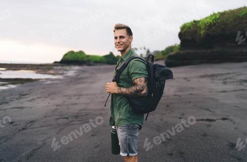 Preview: Cheerful young man with backpack standing on beach