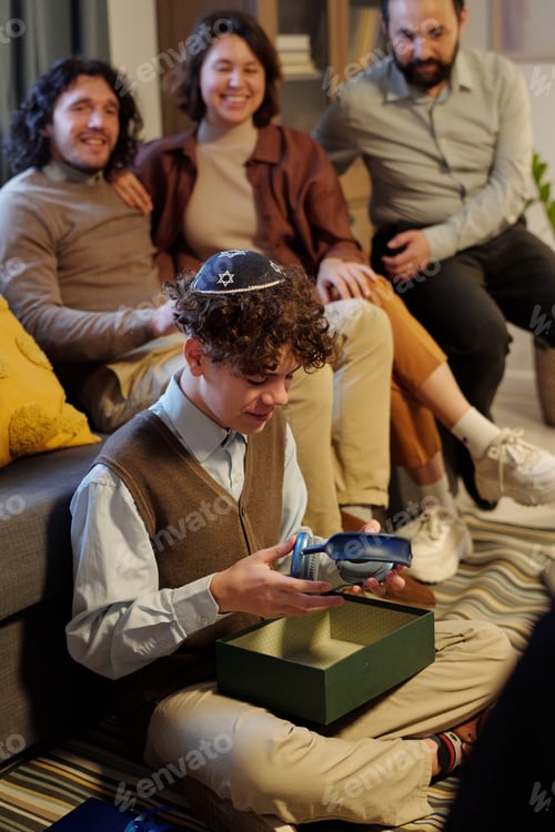 Preview: Pre-teen Jewish boy with headphones unpacking giftbox with Hanukkah present