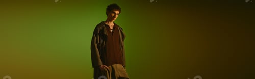 Preview: Young man showcases modern fashion and style against a vibrant green backdrop in creative setting