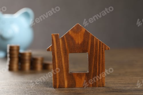 Preview: House model, piggy bank and stacked coins on wooden table, selective focus