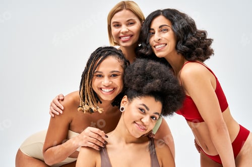 Preview: Positive multiethnic women in colorful and modern lingerie looking at camera while posing together