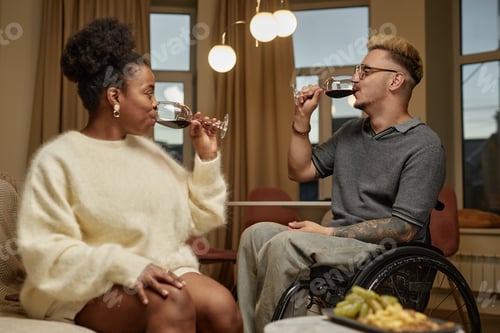 Preview: Man Using Wheelchair Enjoying Wine on Date with Black Woman at Home