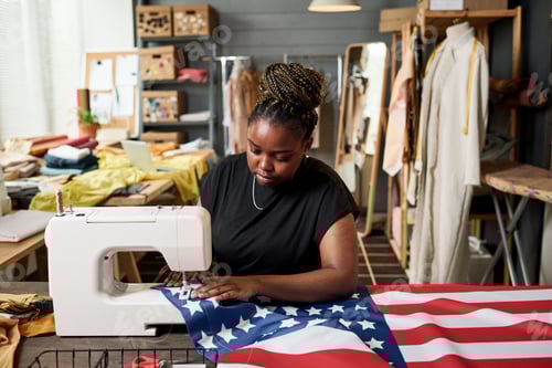 Preview: Young African American female volunteer sewing USA flag on electric machine