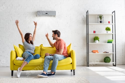 Preview: happy man and woman talking while sitting on yellow sofa under air conditioner at home
