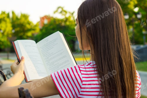 Preview: Attractive woman in red and white t-shirt enjoying a book on the bench in the park