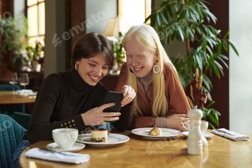 Preview: Two young cheerful girlfriends discussing online photo or video in mobile phone