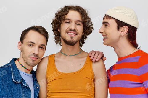 Preview: joyous young gay men in vibrant attires posing together on gray backdrop and looking at camera