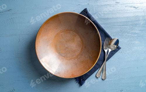 Preview: Top view of a plate with a fork and a spoon on a blue wooden table