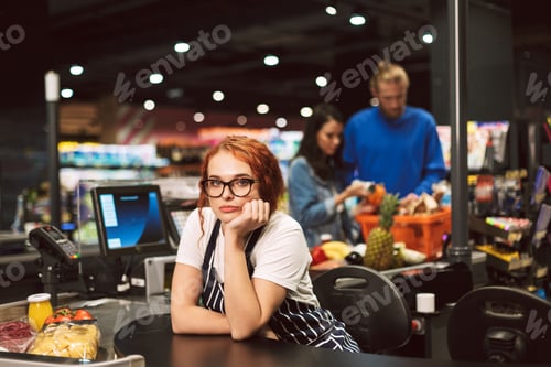 Preview: Young boring cashier in eyeglasses and striped apron thoughtfull