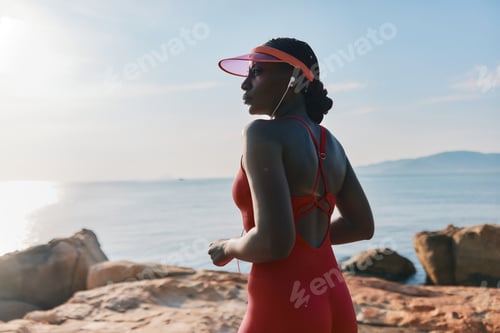 Preview: A woman runs along the rocky beach during sunset, wearing a vibrant red athletic outfit and