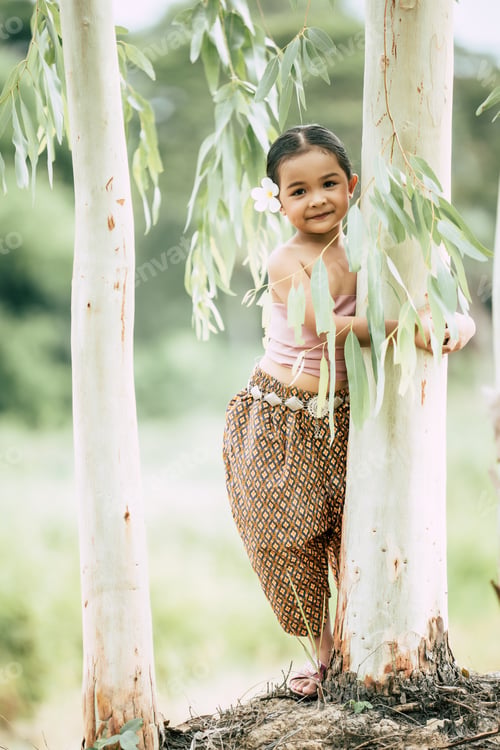 Preview: little girl in Thai traditional dress Embrace trunk of tree