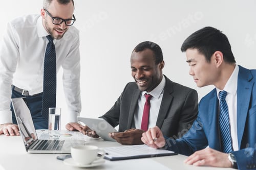 Preview: multicultural smiling businessmen using tablet together during meeting at workplace